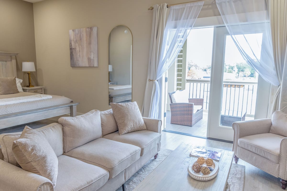 A spacious living area with a sofa, armchairs, a coffee table, and a balcony with a view.