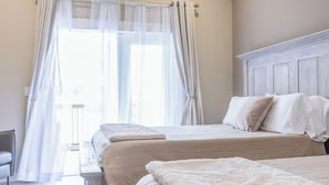 Un dormitorio con dos camas, cabecero de madera y cortinas translúcidas.