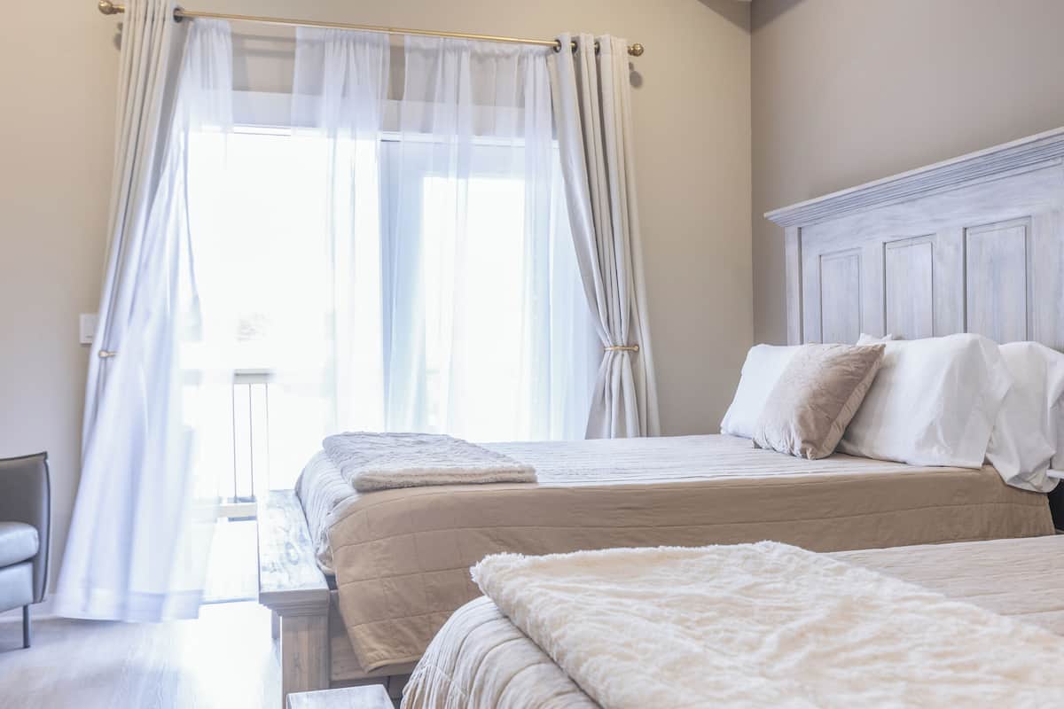 A bedroom with two beds, a wooden headboard, and sheer curtains.