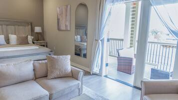 Quarto de hotel com cama, sofá, mesa de cabeceira, luminária, espelho e varanda com mobiliário de vime.