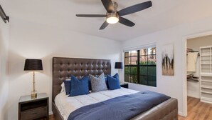 A bedroom with a tufted headboard, a bed with blue bedding, a nightstand with a lamp, a ceiling fan, and a window with a view of greenery. - Premier location in Scottsdale close to Old town & Open- HEATED pool & jacuzzi😎 (Paradise Valley)