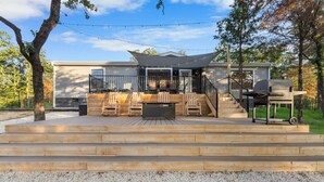 Un terrazzo in legno con mobili da esterno, un barbecue e una zona coperta con luci a stringa.