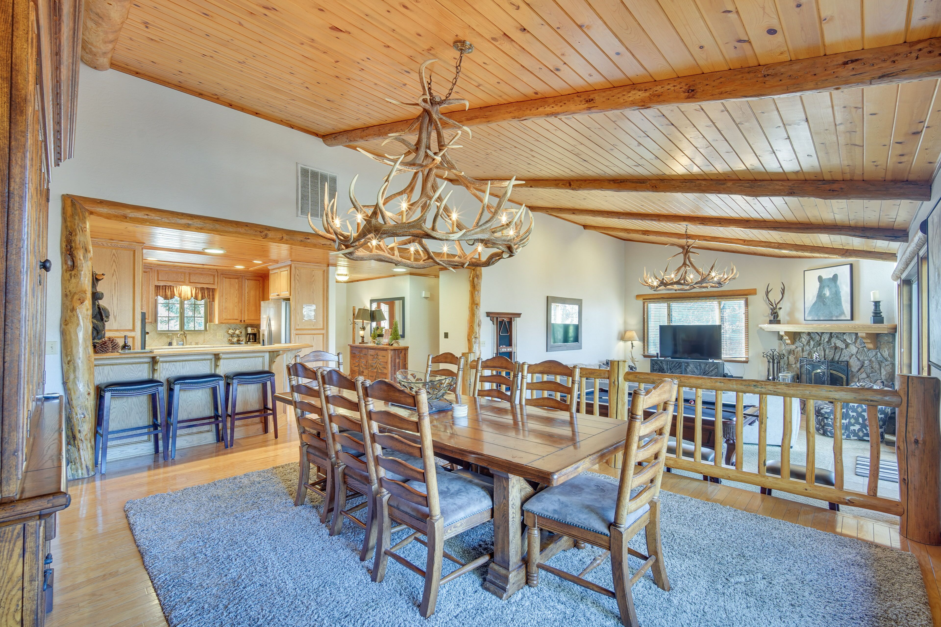 Un vaste espace dédié à la salle à manger, avec une grande table et des chaises en bois, un lustre, et une vue sur la cuisine et le salon.