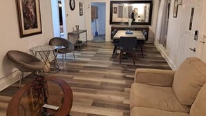 A modern living room with a wooden floor, a round coffee table, a sofa, and a dining area with a table and chairs.