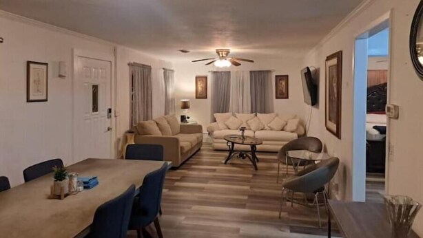 A spacious living room with a dining area, a ceiling fan, and a TV mounted on the wall.