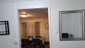 A room with a dining area featuring a table and chairs, a mirror on the wall, and a ceiling light.