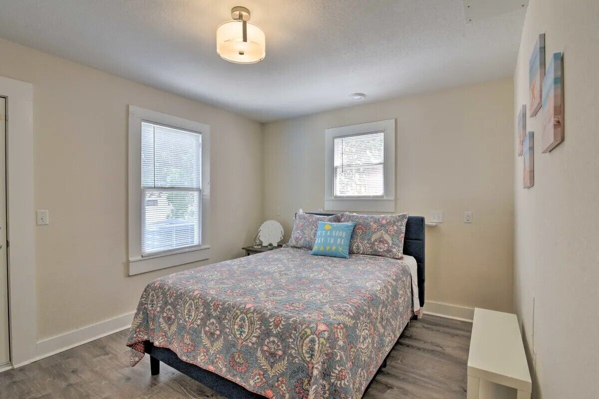 A bedroom with a bed, two windows, a nightstand, and a bedside table.