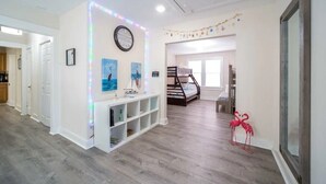 Una habitación amplia con una litera, una consola blanca con libros y un reloj en la pared.
