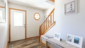 Un pasillo con una escalera de madera, una puerta y un aplique en la pared.