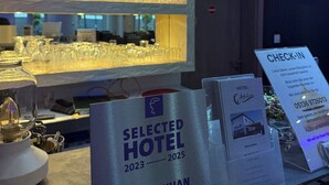 Un espace d’accueil d’hôtel où sont exposées une sélection de bouteilles d’alcool et des verres. On peut y voir des panneaux indiquant le comptoir d’enregistrement et des brochures sur l’hôtel.