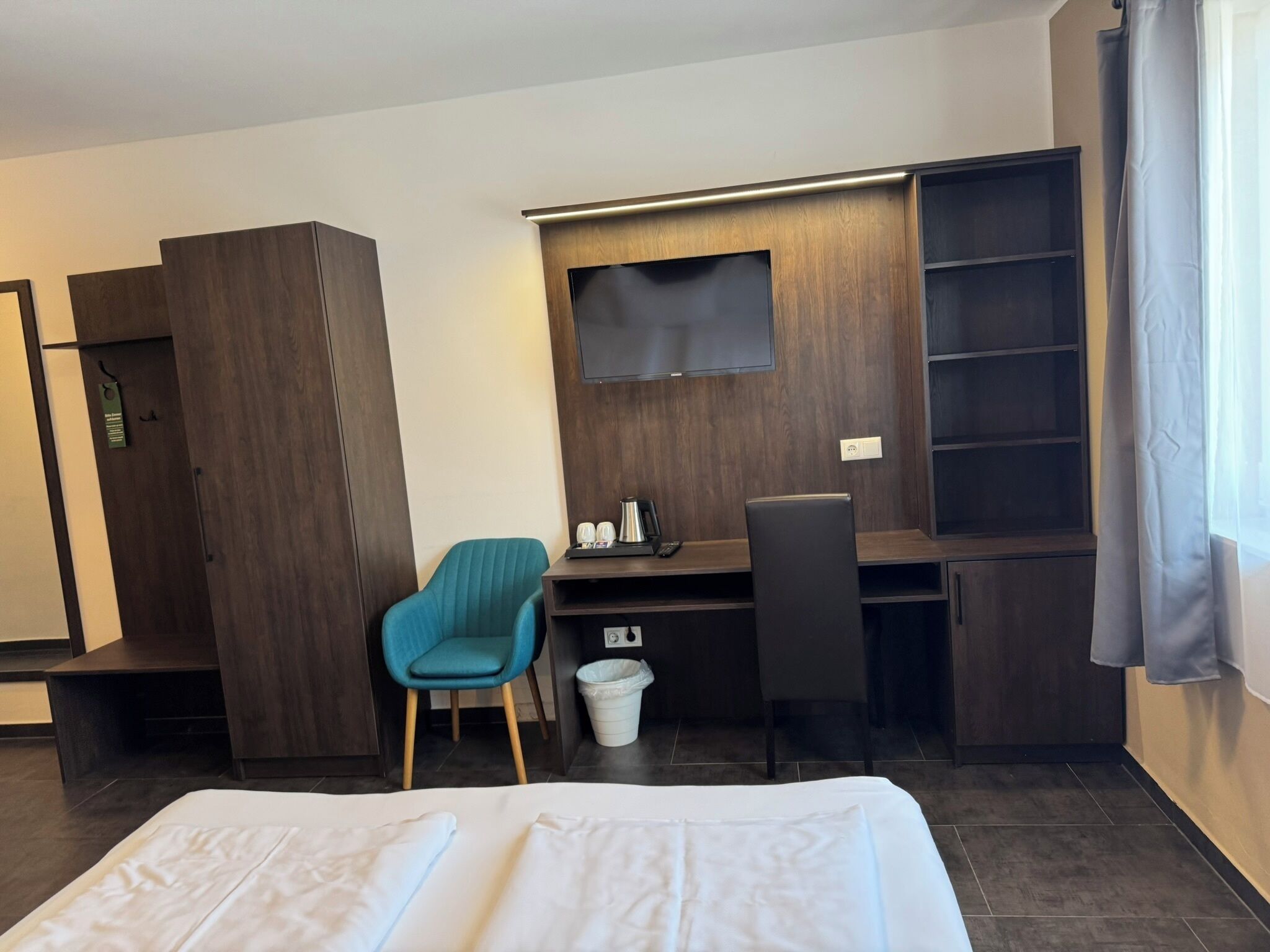 A hotel room with a bed, a desk, a chair, a TV, and a wardrobe.
