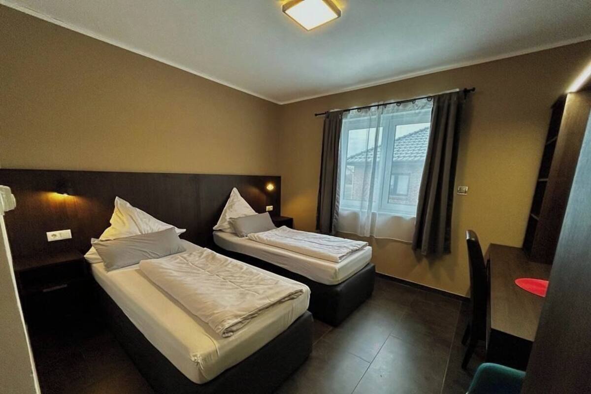 A hotel room with two single beds, a small desk, and a window with curtains.