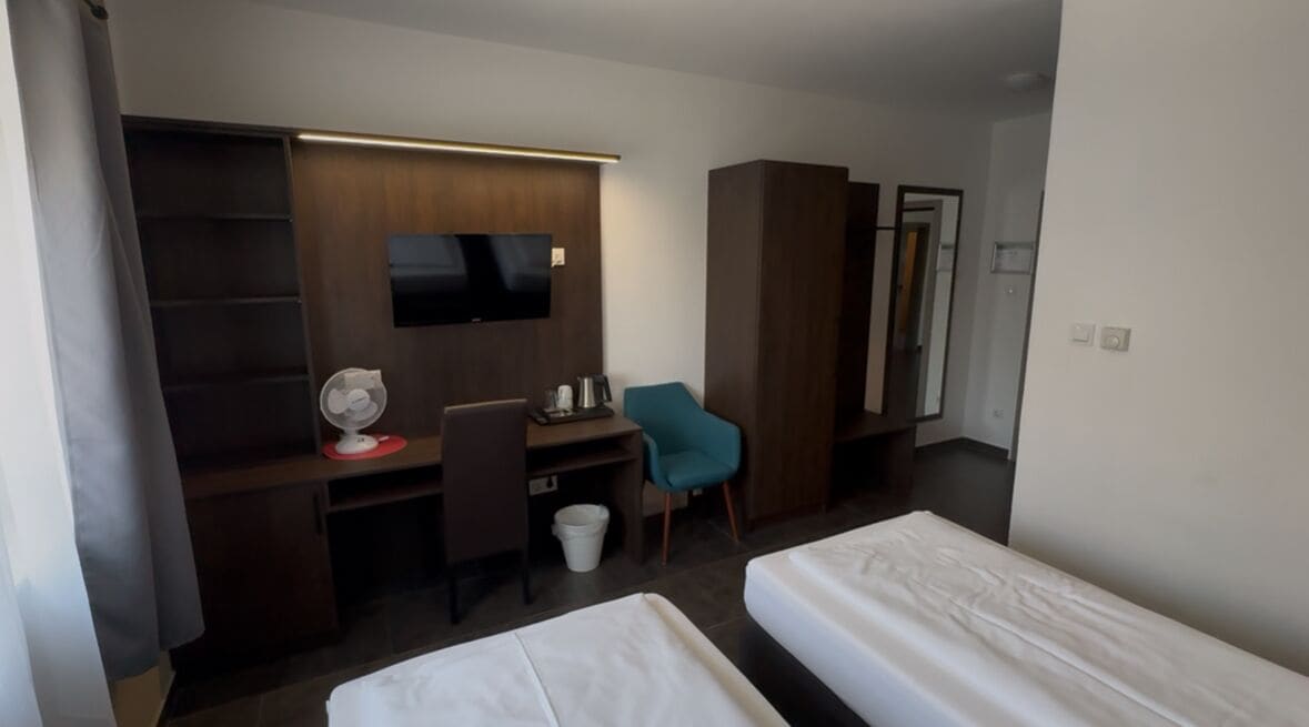 Una habitación de hotel con cama, escritorio, silla, televisor y armario.