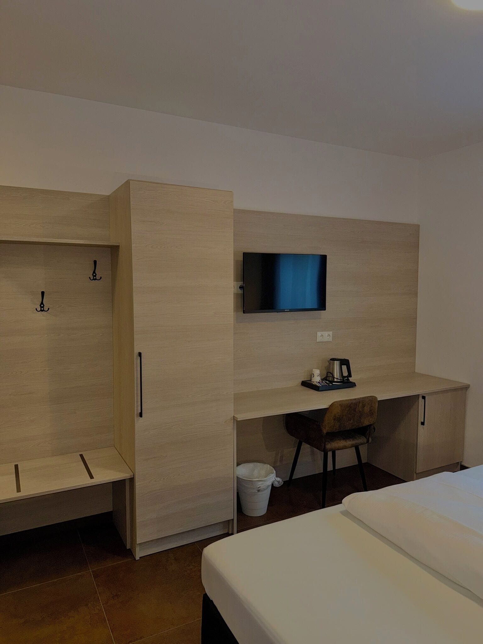 A hotel room with a bed, a desk with a television, a chair, and a wardrobe.
