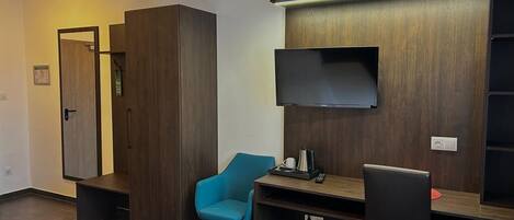 A compact room with a bed, a desk with a chair, a television, and a wardrobe.