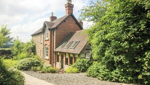 A traditional brick house with a sloped roof, large windows, and a well-maintained garden with gravel paths. - Wayside House (Craven Arms)