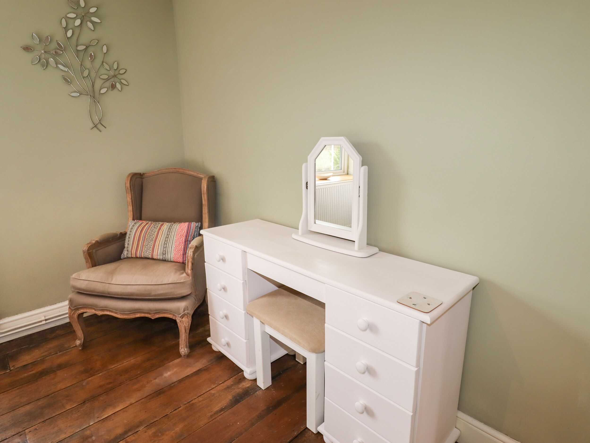 Een kamer met een houten stoel, een witte dressoir met lades en een spiegel aan de muur.