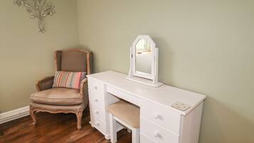 Een kamer met een houten stoel, een witte dressoir met lades en een spiegel aan de muur.