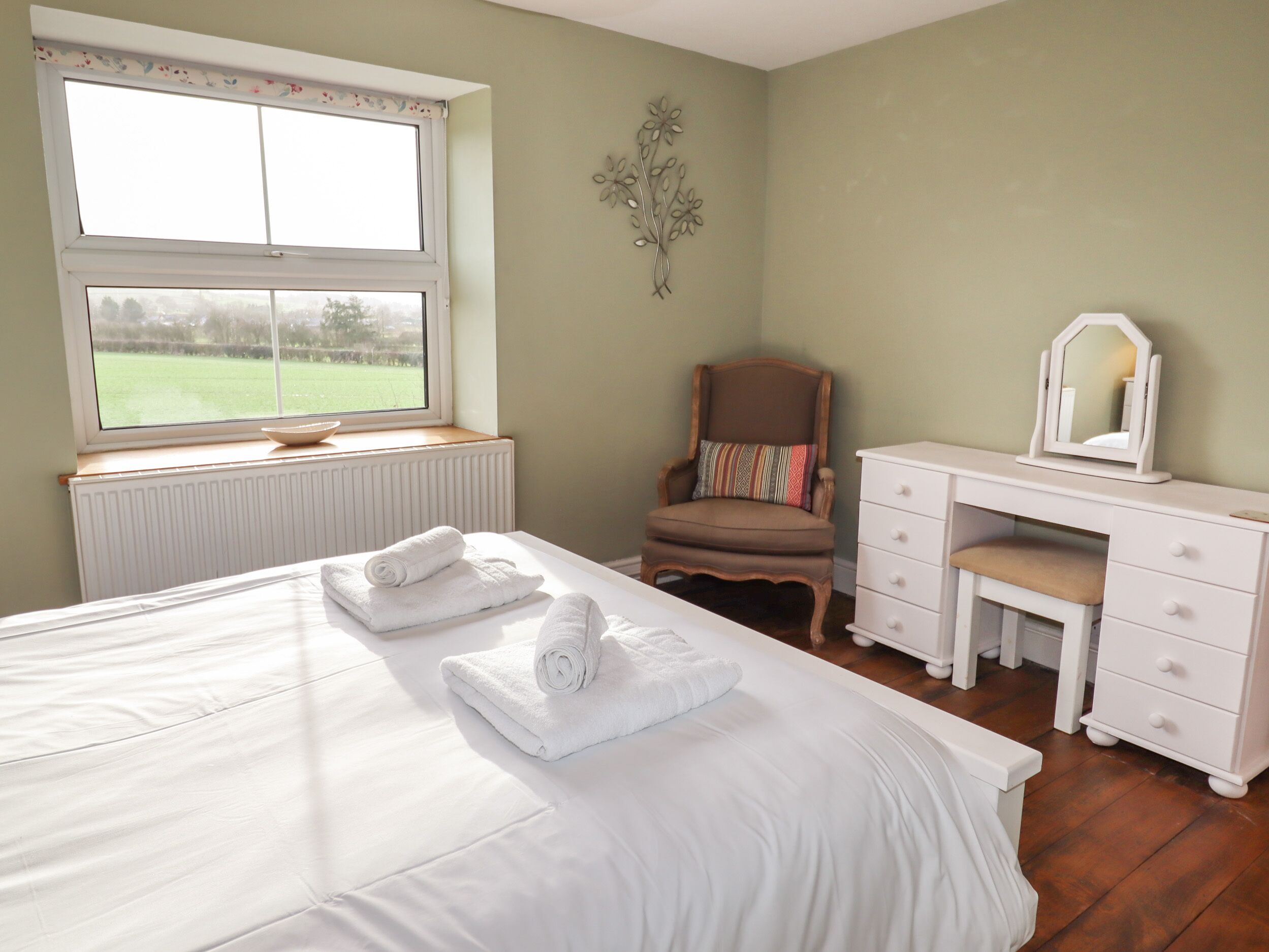 A bedroom with a bed, a chair, a dresser, and a window with a view of a green field.