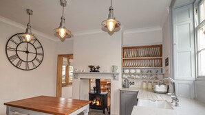 A kitchen with a wooden table, a white countertop, a fireplace, and a clock on the wall. - Wayside House (Craven Arms)