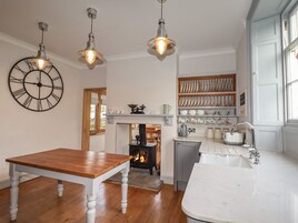 A kitchen with a wooden table, a white countertop, a fireplace, and a clock on the wall.