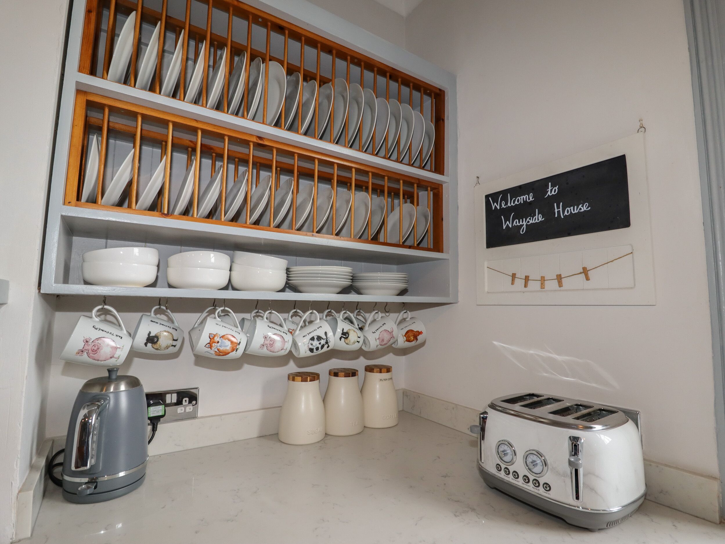 Une cuisine équipée d’un égouttoir, d’une bouilloire, d’un grille-pain et d’une pancarte sur laquelle on peut lire : « Bienvenue à WAYSIDE HOUSE ».