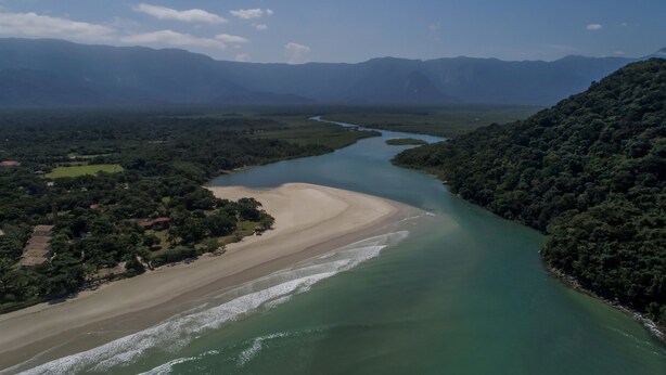 Paisaje costero con río, playa y colinas boscosas.