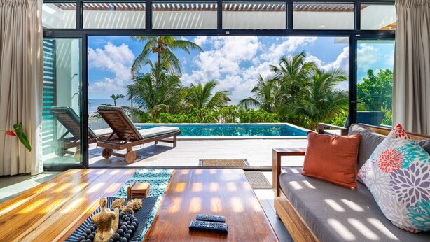 Une chambre moderne dotée d’une grande baie vitrée donnant sur une piscine et des palmiers.