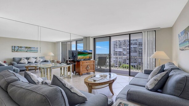 Una sala moderna con un conjunto de sofás, una mesa de centro, un televisor y un balcón con vistas a la ciudad.
