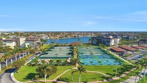 Un resort con varias canchas de tenis, una piscina y vistas de la ciudad circundante.