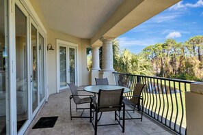 A balcony with a round table and chairs, glass doors, and a view of trees and a water feature.