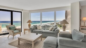 Ein geräumiges Wohnzimmer mit großem Fenster und Meerblick, ausgestattet mit einer Couch, Sesseln und einem Couchtisch.