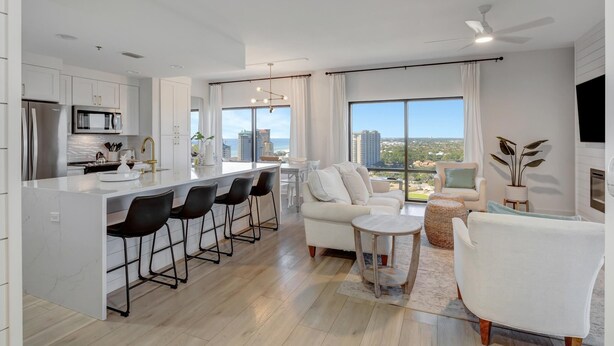 A modern kitchen with a central island, bar stools, and a dining area with a white sofa and chairs.