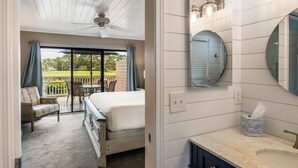 A hotel room with a bed, a balcony with a view of a golf course, a ceiling fan, and a bathroom with a mirror and sink. - Breathtaking Balcony Views: Spacious 2-Bed, 2-Bath Condo for 4 (Miramar Beach)