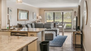 A modern kitchen with a marble countertop, a dining area with a table and chairs, and a large window with blinds. - Breathtaking Balcony Views: Spacious 2-Bed, 2-Bath Condo for 4 (Miramar Beach)