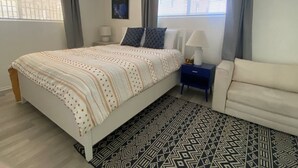 Une chambre à coucher avec un lit, une table de chevet, une lampe, un canapé et un tapis à motifs.