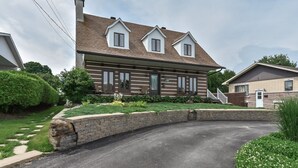 A two-story log cabin with a front porch, a brick driveway, and a well-maintained lawn. - Charmante, spacieuse maison canadienne/Charming and very spacious Canadian house (Saint-Jérôme)