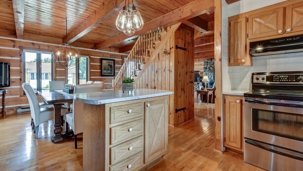 A spacious kitchen with wooden cabinets, a large island with drawers, a built-in oven, and a staircase leading to another level. - Charmante, spacieuse maison canadienne/Charming and very spacious Canadian house (Saint-Jérôme)