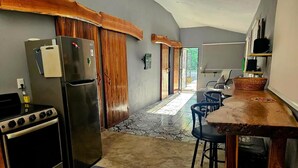 A compact kitchen with a refrigerator, stove, and bar stools. - Casa Cariad *Cottage house near Playa Bejuco*

 (Provincia de Puntarenas)