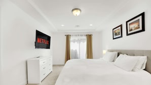 Quarto de hotel com uma cama grande, uma TV fixada na parede e uma janela com cortinas.