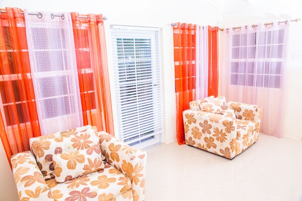 A room with two sofas, a window with blinds, and orange curtains. - Areca Homes in Draxhall (St. Ann's Bay)