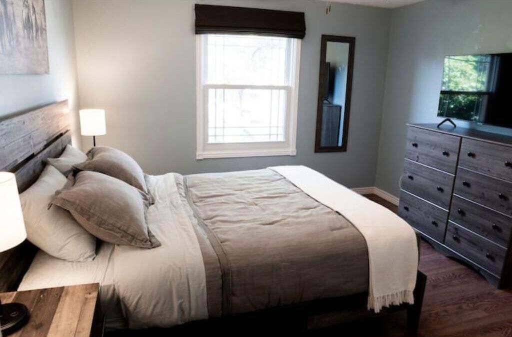 A bedroom with a bed, a dresser, a window, and a lamp.