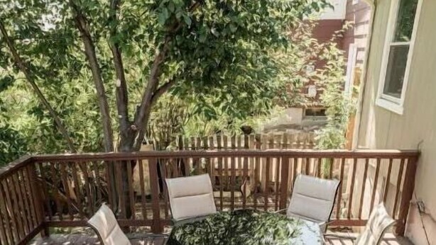 Une terrasse en bois avec une table et des chaises à plateau en verre, entourée d’une clôture en bois.