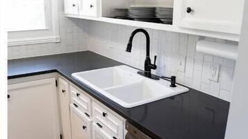 Cocina moderna con armarios blancos, encimera negra, lavavajillas de acero inoxidable y grifo negro.