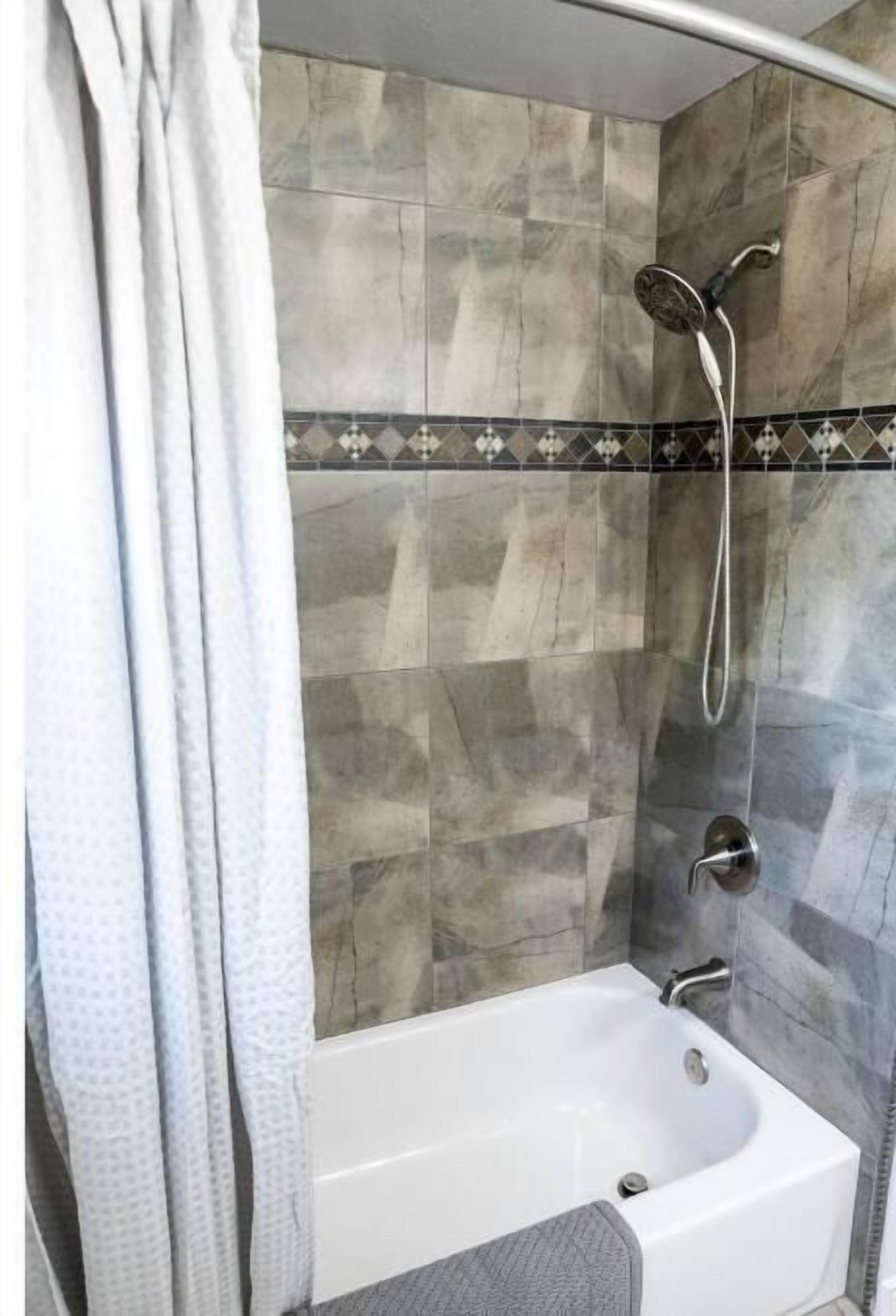 Ein Badezimmer mit einer Badewanne, einer Dusche und einer gefliesten Wand.