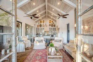 Relax in this spacious living area with a central seating area, sofas, and armchairs, plus a large mirror and kitchen in the background.