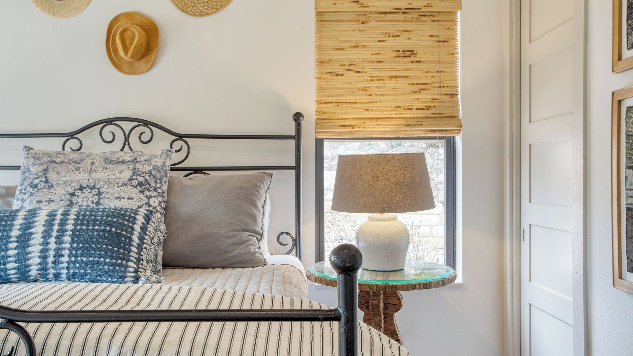 A bed with patterned pillows, a bedside table with a lamp, and a window with a bamboo blind.