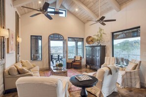 Relax in this inviting living area with a high ceiling, ceiling fans, and a large window offering a view of the outdoors.