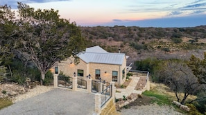 A stone building with a metal roof, surrounded by trees and a hilly landscape. - Sotol by Avantstay Direct River Access + Views (Dripping Springs)