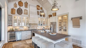 A kitchen with a central island, white cabinetry, and a rustic ceiling. - Sotol by Avantstay Direct River Access + Views (Dripping Springs)